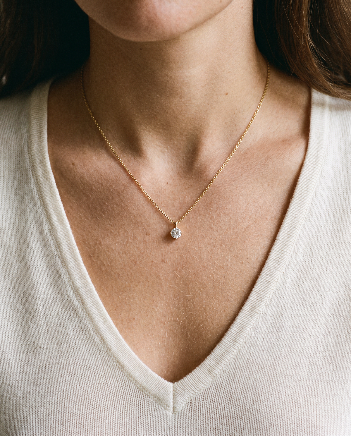 Gold prong set solitaire necklace resting inside the V of an ivory knit neckline