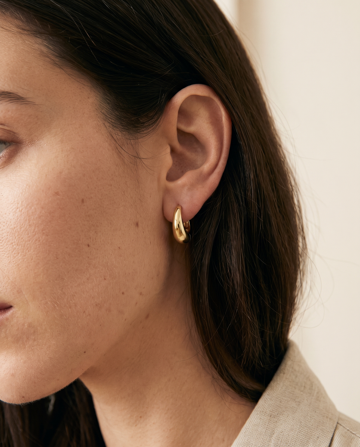 Woman wearing a gold dome huggie earring in soft morning light