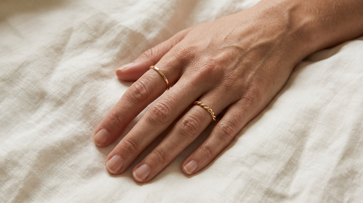 Hand wearing a thin hammered gold band and a gold twisted rope ring with bare fingers between them